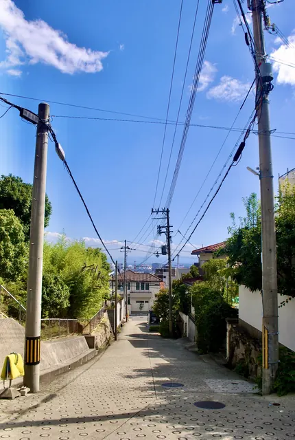 左右に立つ電柱と電線のあいだを、町へ下っていく坂道