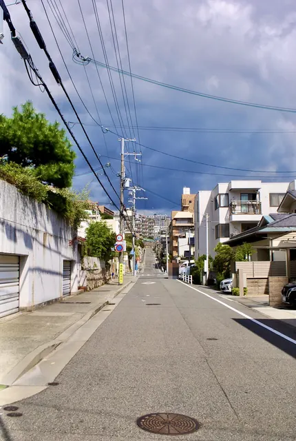 暗い雨雲と電線の下、住宅のあいだをまっすぐ上っていく坂道