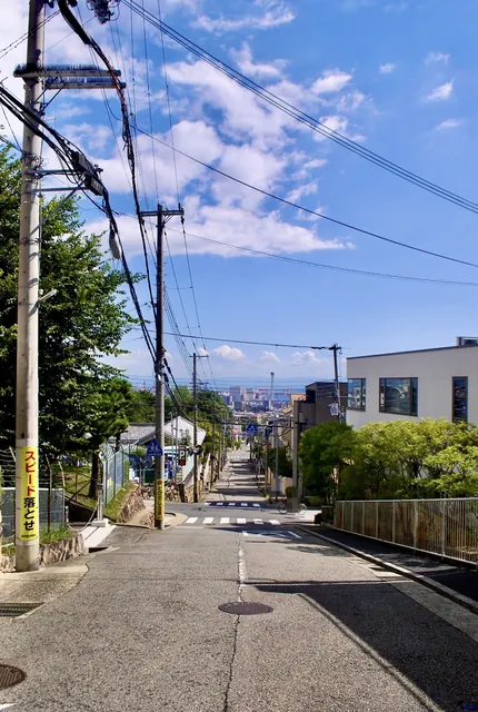 電線の張られた空の下、遠くの町並みまでまっすぐ下っていく坂道