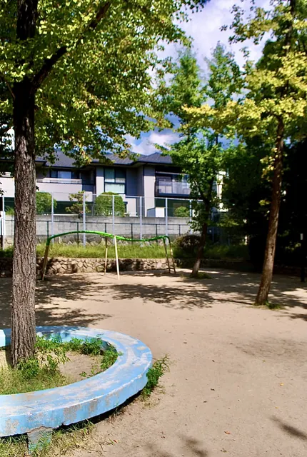 大きな木の下に、丸いベンチと遊具のある公園