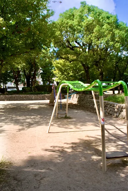大きな木々の下に、緑色の遊具が立つ公園