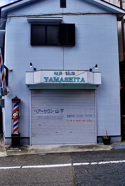 青い壁の建物に、シャッターとサインポールのある理容店