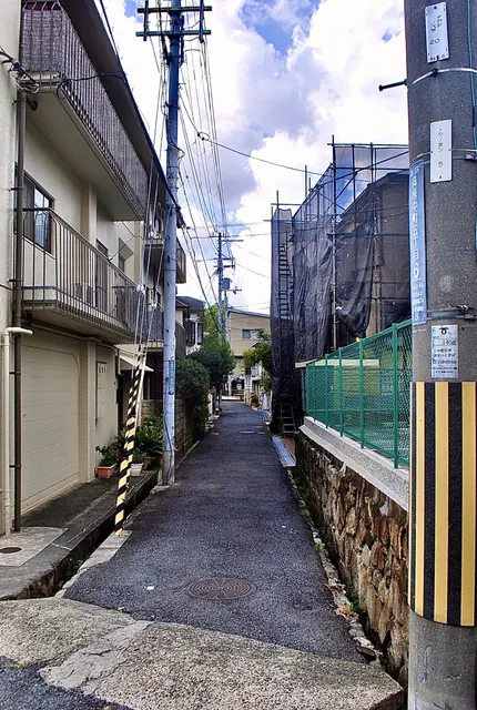 町名表示のある電柱の脇から、石垣に沿って続く細い路地