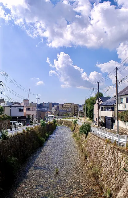 大きな雲の浮かぶ青空の下、石積みの川がまっすぐ続く風景