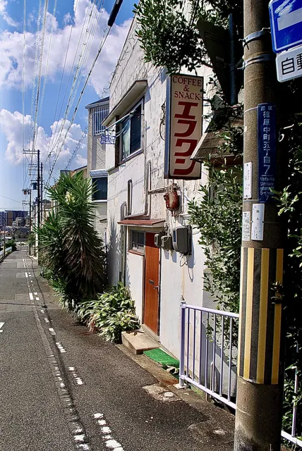 縦長の看板と赤い扉のある、白い外壁の店先