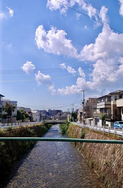 川を横切るパイプの向こうに、住宅と青空が見える風景