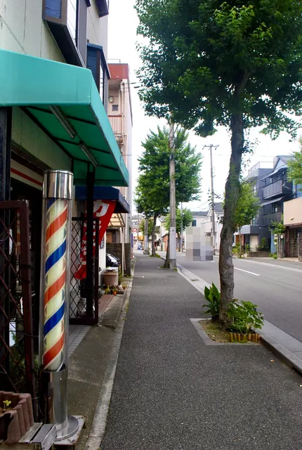 赤白青のサインポールの理容店から、並木の続く大通りの歩道