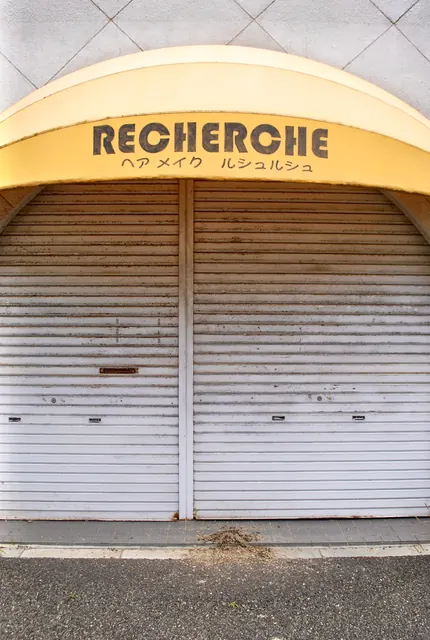 黄色い丸いひさしに「RECHERCHE」の文字がある、シャッターの美容室