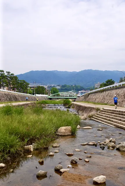 石が並ぶ浅い川の流れの先に、山並みと橋が見える風景