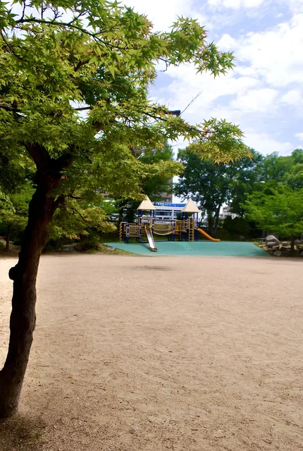 木の枝の向こうに、遊具が見える砂地の公園