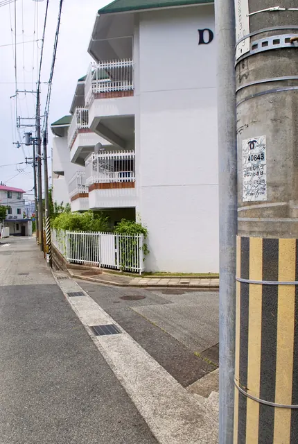白い壁のマンションと電柱の並ぶ、静かな坂道