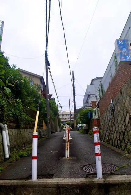紅白の車止めが立ち、石垣とレンガの壁のあいだを上る坂道