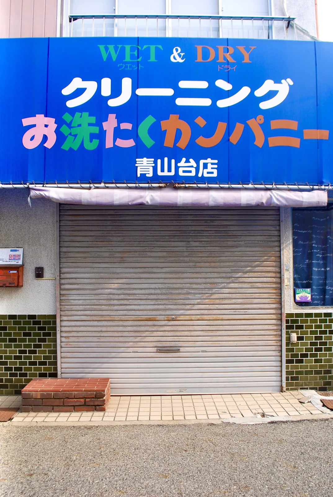 カラフルな文字の看板と、シャッターの閉まったクリーニング店
