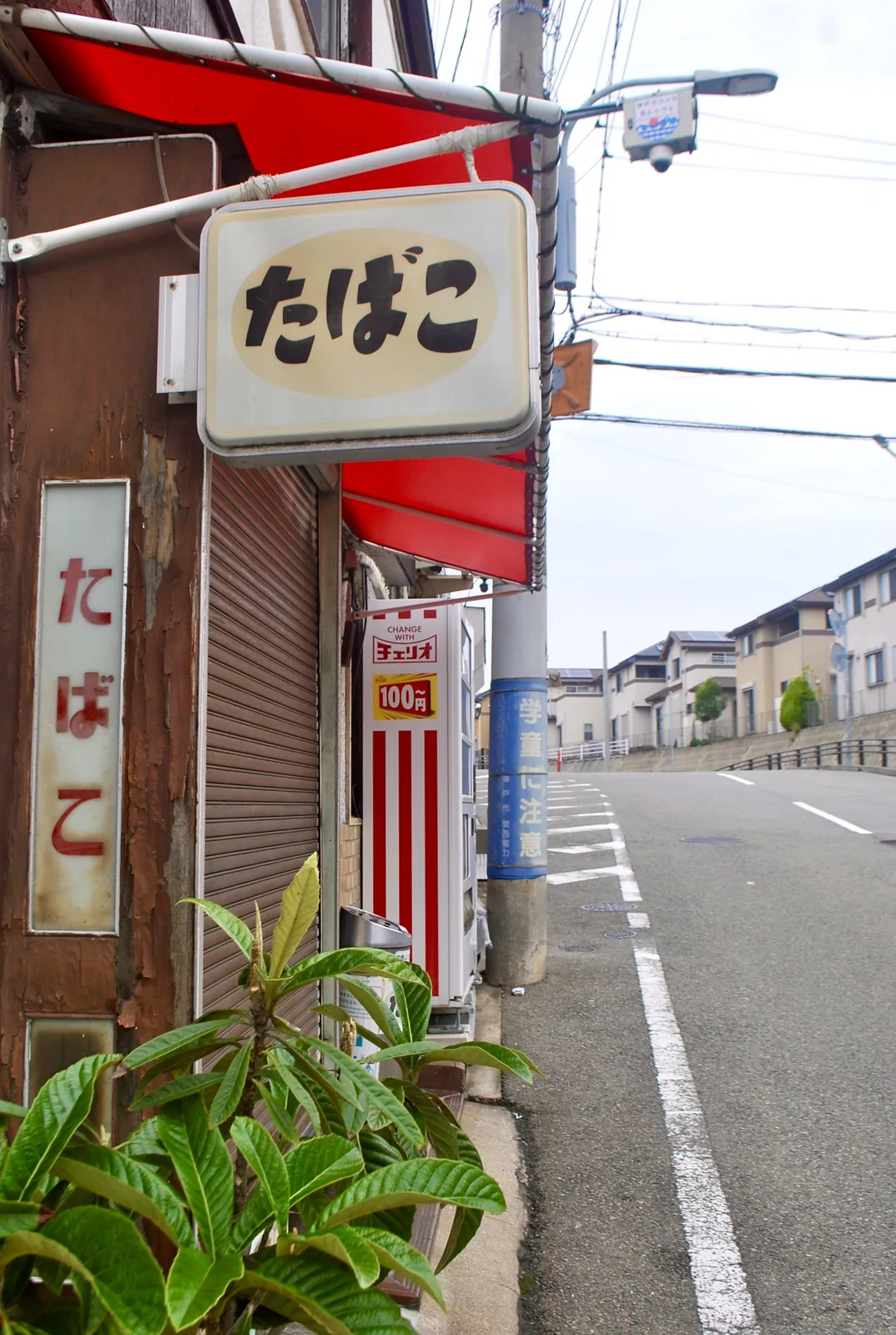「たばこ」の看板と赤い日よけ、自動販売機の並ぶ店先