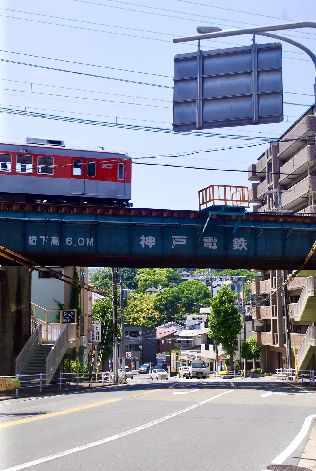 通りの上に架かる鉄橋を、赤い電車が渡っていく風景