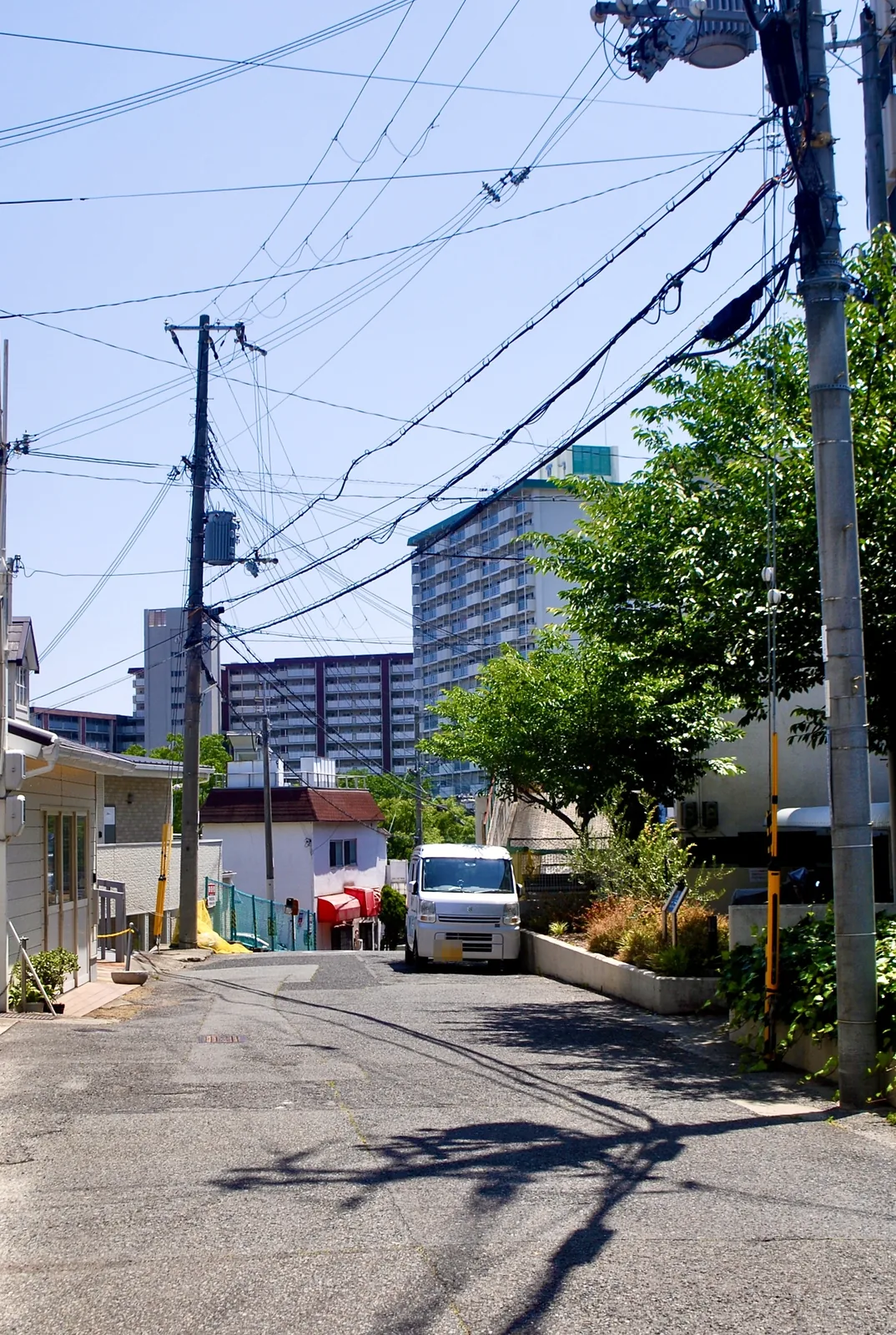 電線の張られた坂道の先に、住宅と大きな団地が見える風景