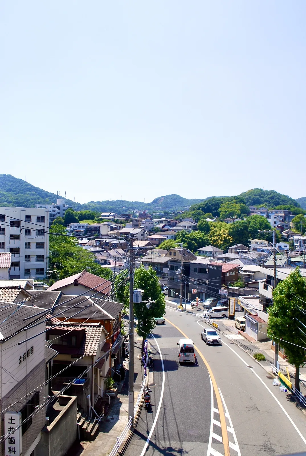 高いところから、山に囲まれた町並みとカーブする道を見下ろす風景