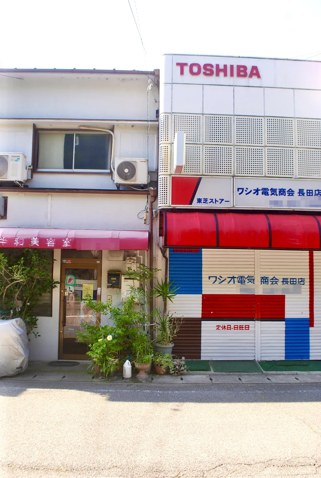 赤いテントの電気店と、ピンクの日よけの美容室が並ぶ店先