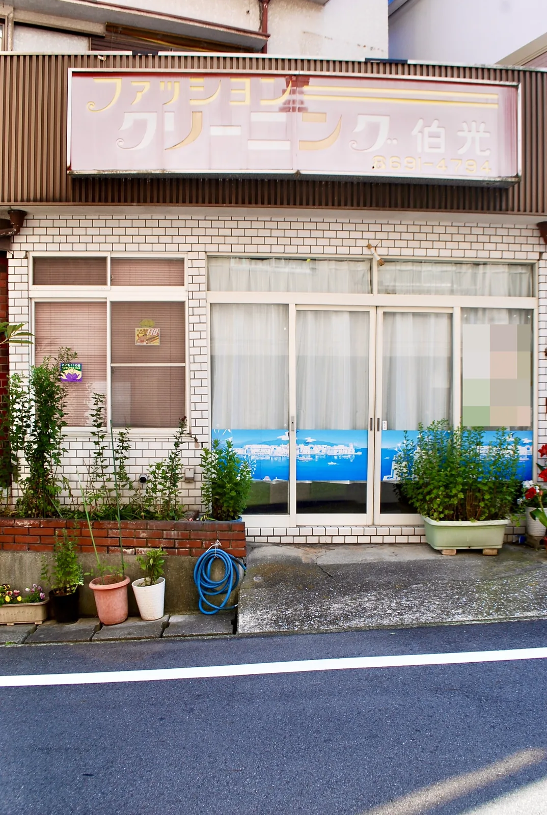 色あせたクリーニング店の看板と、植木鉢の並ぶ店先