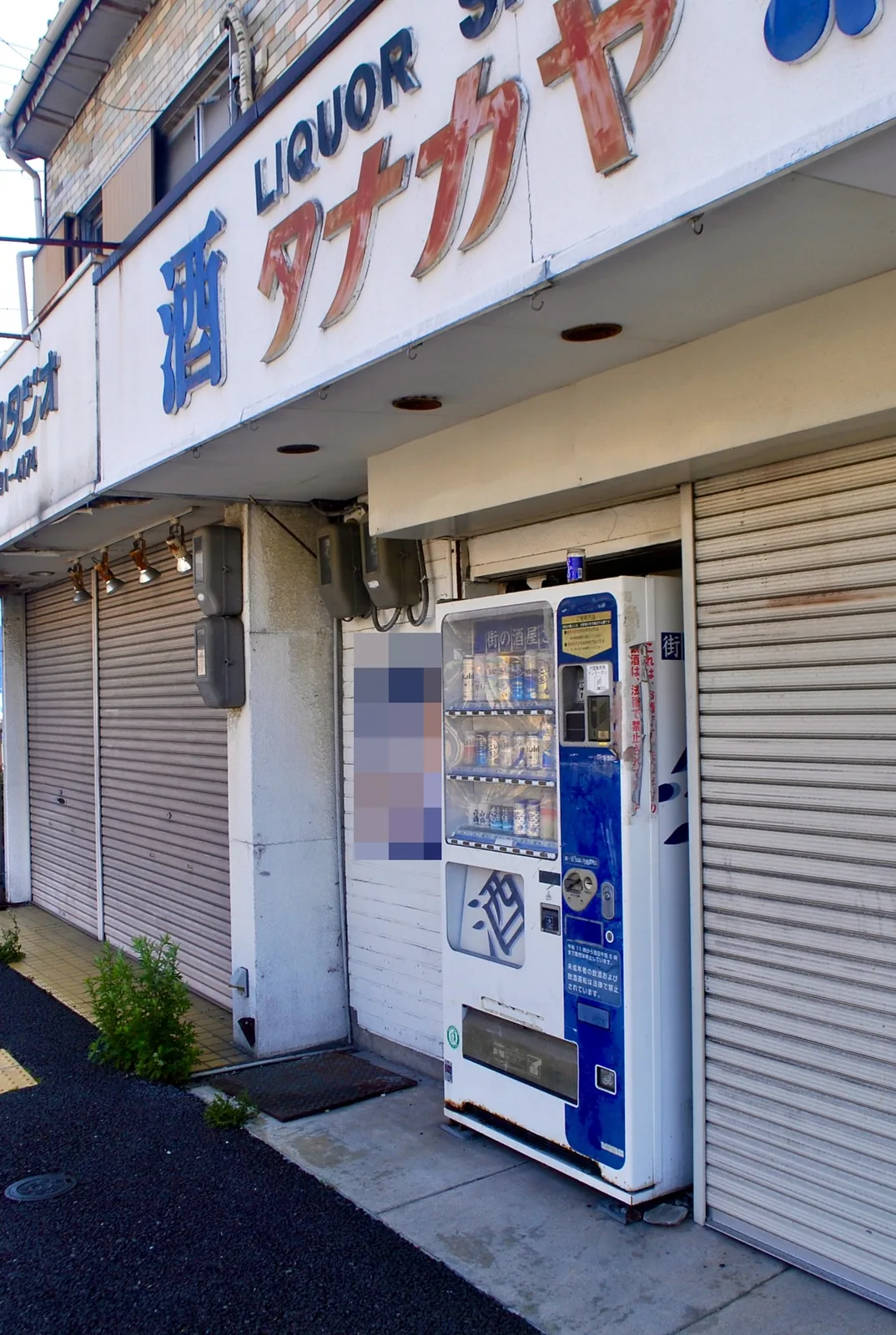 大きな文字の看板と自動販売機のある、角の酒店