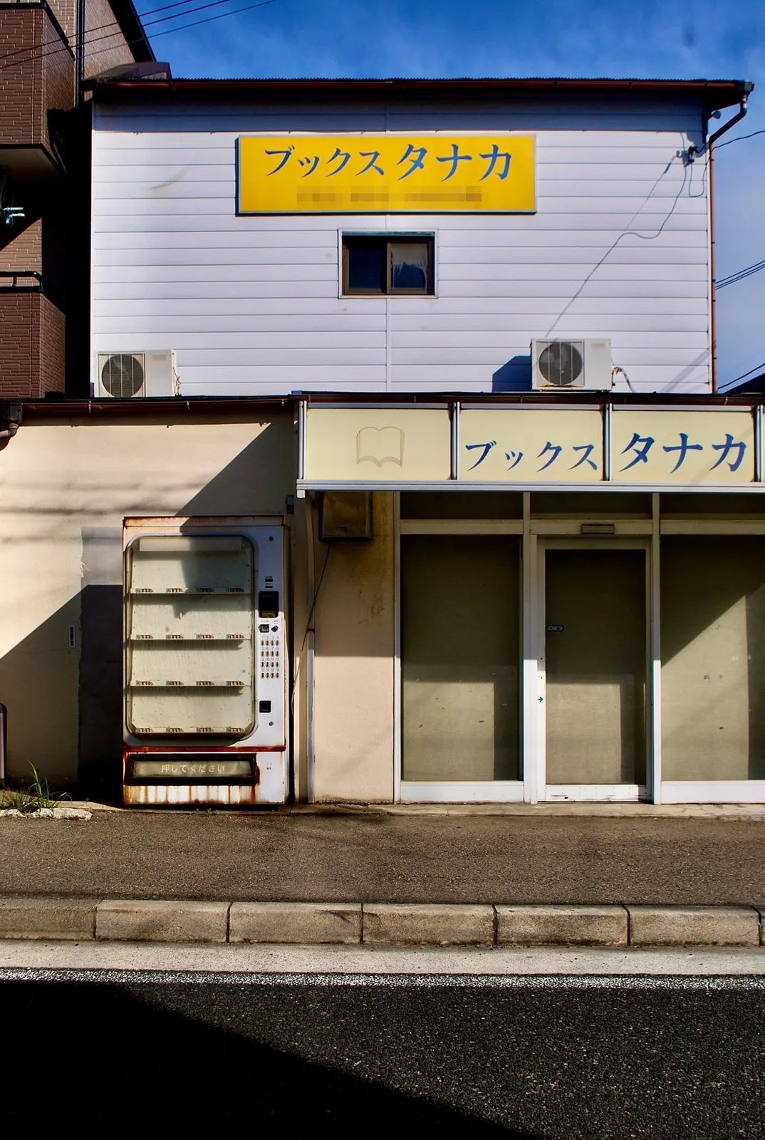 黄色い看板の建物と、古い自動販売機のある店先
