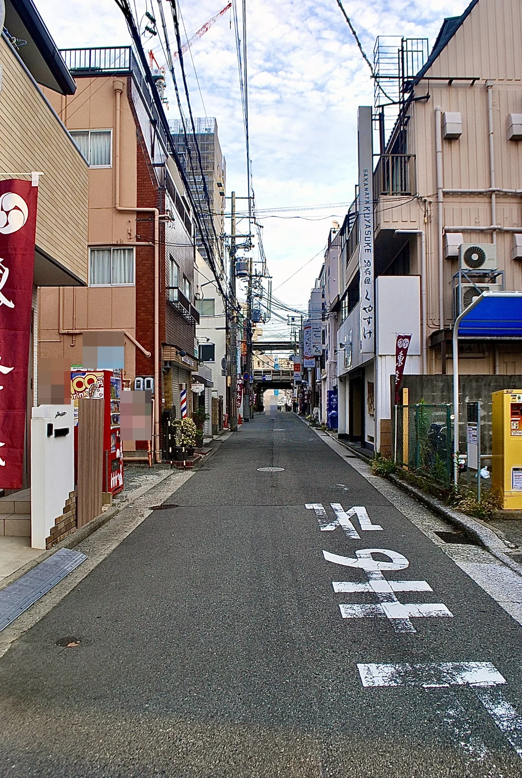 店の看板やのぼりが並び、奥に高架の見えるまっすぐな通り