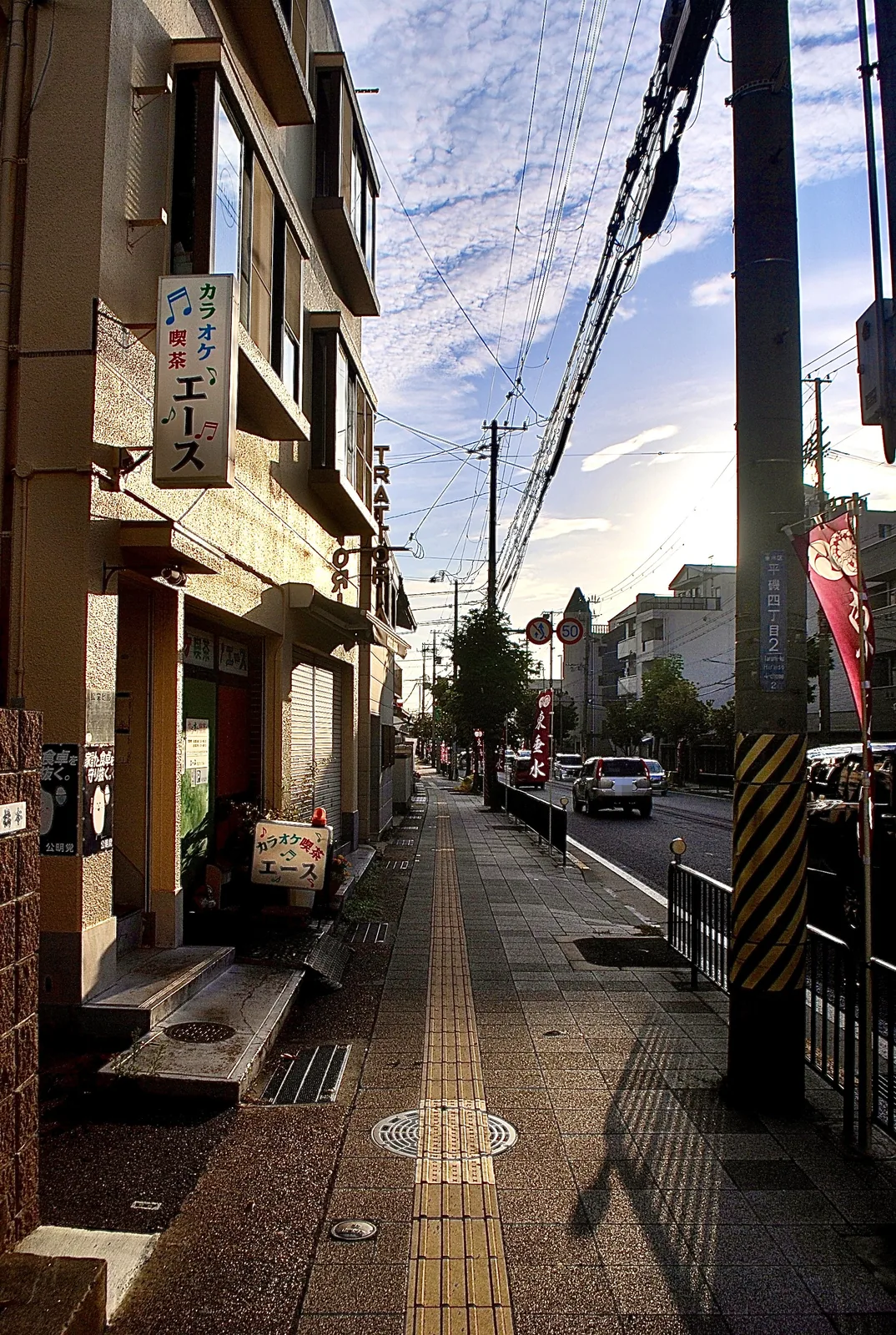 カラオケ喫茶の看板が出た建物と、夕方の光が差す歩道