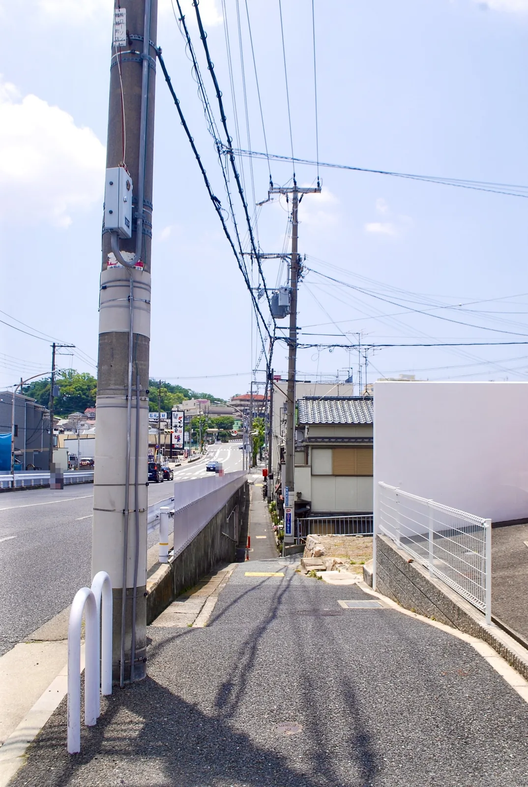 大きな電柱の脇から、電線の下を奥へ続く歩道と大通り