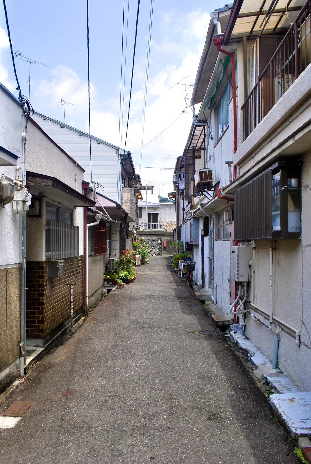古い長屋が並び、植木の置かれた奥の石垣へ続く路地