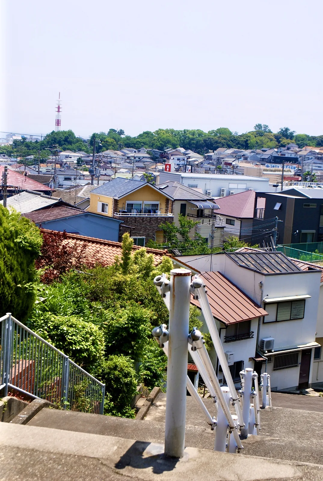 手すりのある坂の上から、屋根の連なる町並みを見下ろす風景