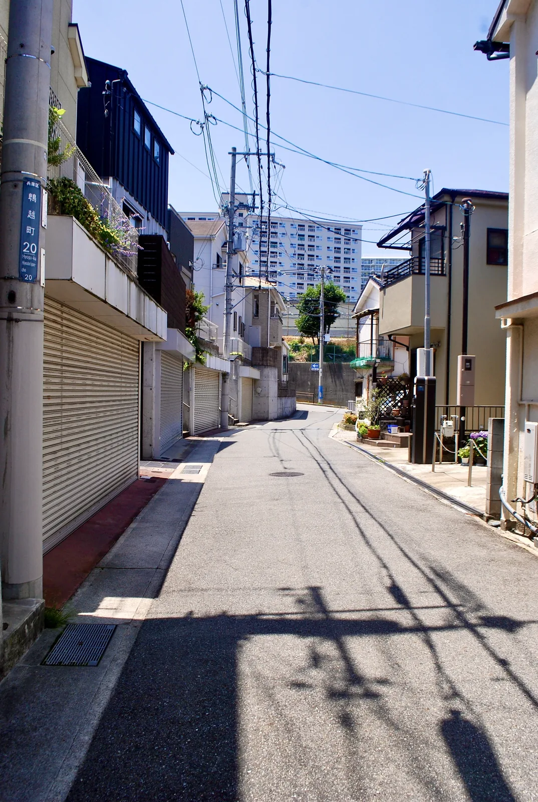 町名表示のある電柱と、シャッターの並ぶ住宅街の通り