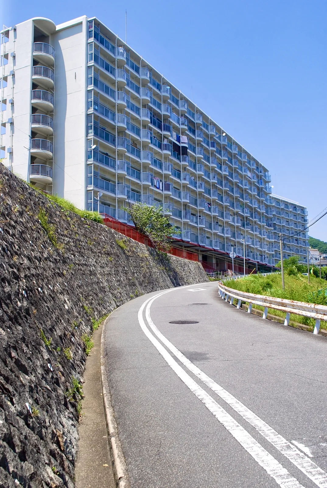 石垣に沿ってカーブする坂道と、その上に長く続く団地
