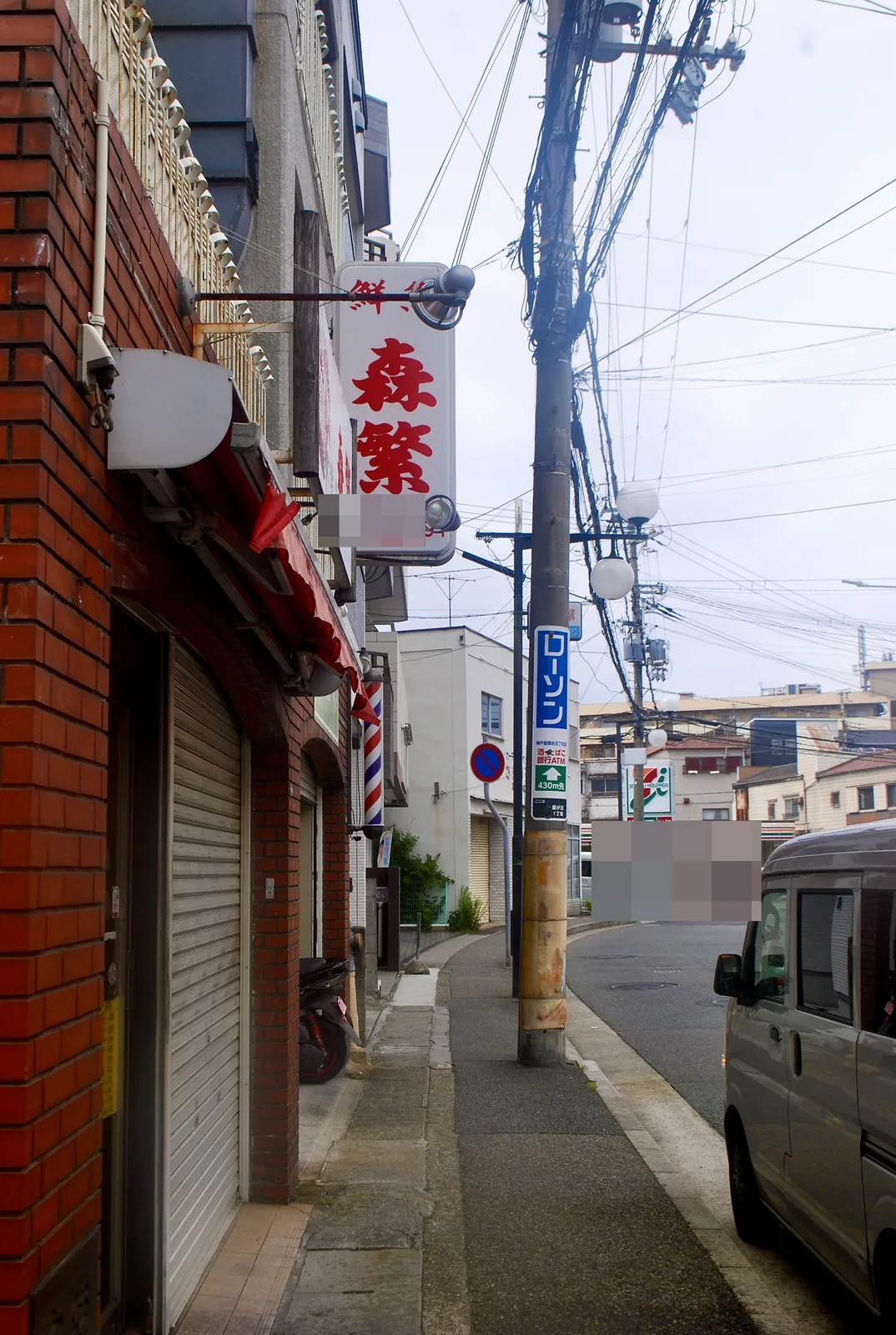 赤い看板とサインポールの並ぶ、シャッターの店の角