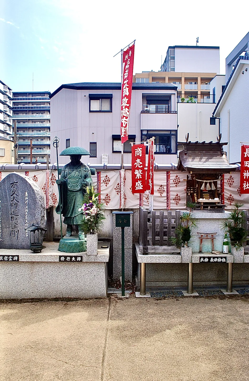 弘法大師の像と、「商売繁盛」ののぼりが立つ小さなお社