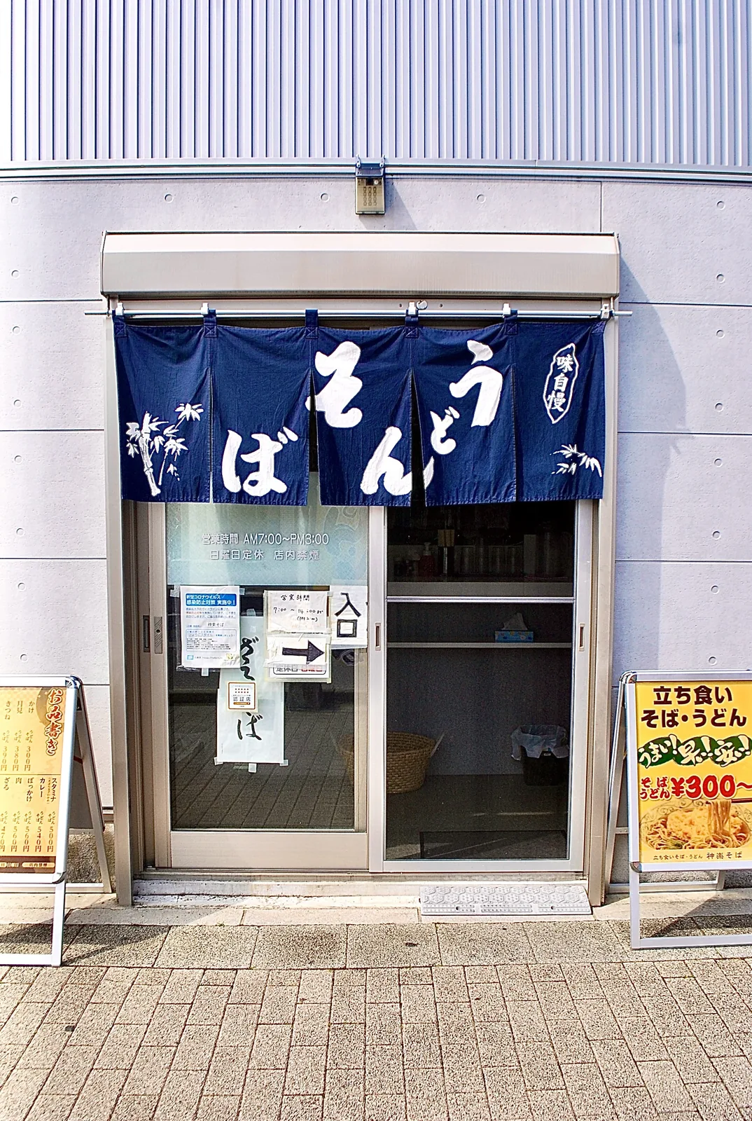 「そば うどん」の紺ののれんと、立て看板が並ぶ店の入口