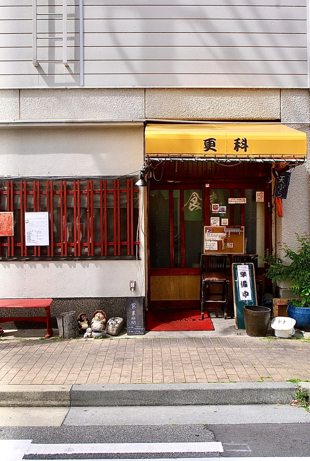 黄色い日よけと赤い格子、たぬきの置物が並ぶそば処の入口