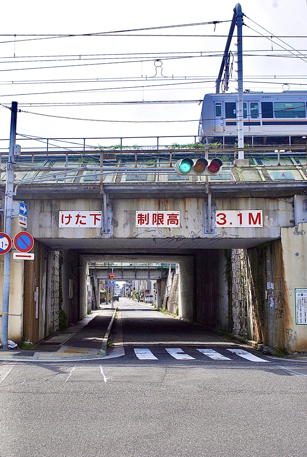 信号の先に、古い高架の下をくぐるトンネルが続く風景