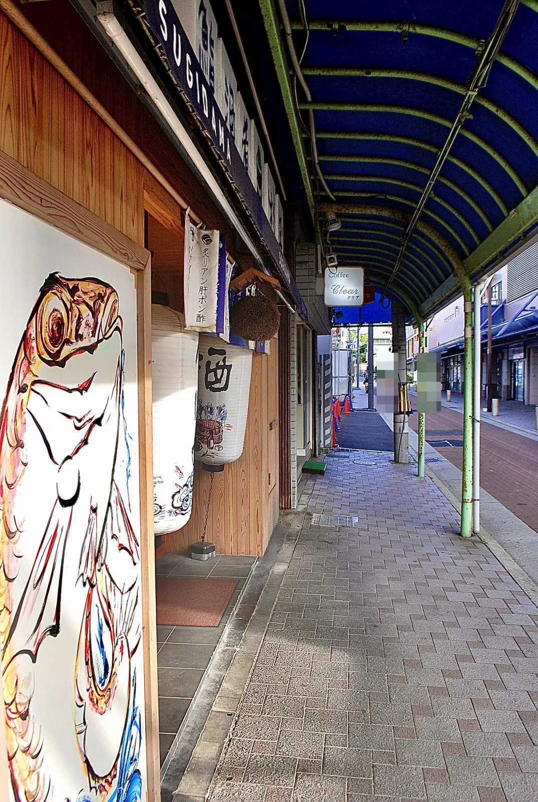 手描きの大きな魚の絵と、「酒」の提灯が下がる居酒屋の入口