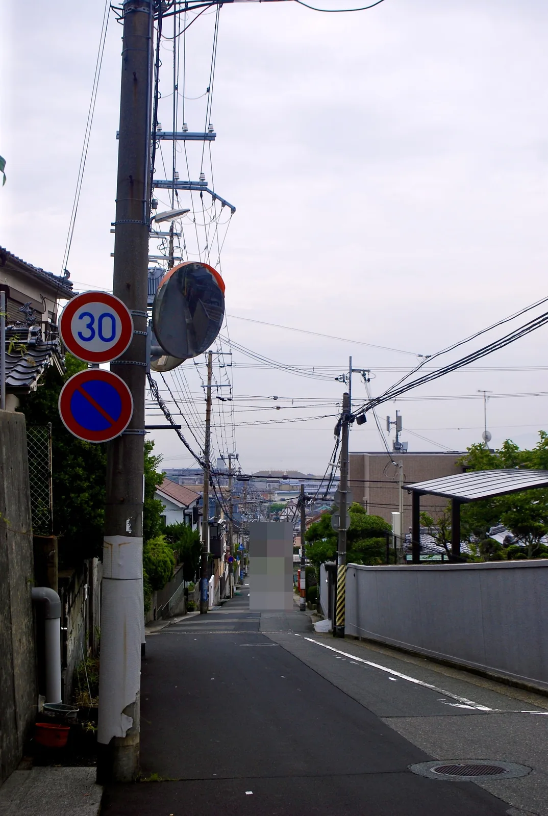 速度標識の立つ坂の上から、遠くの家並みへ下っていく坂道