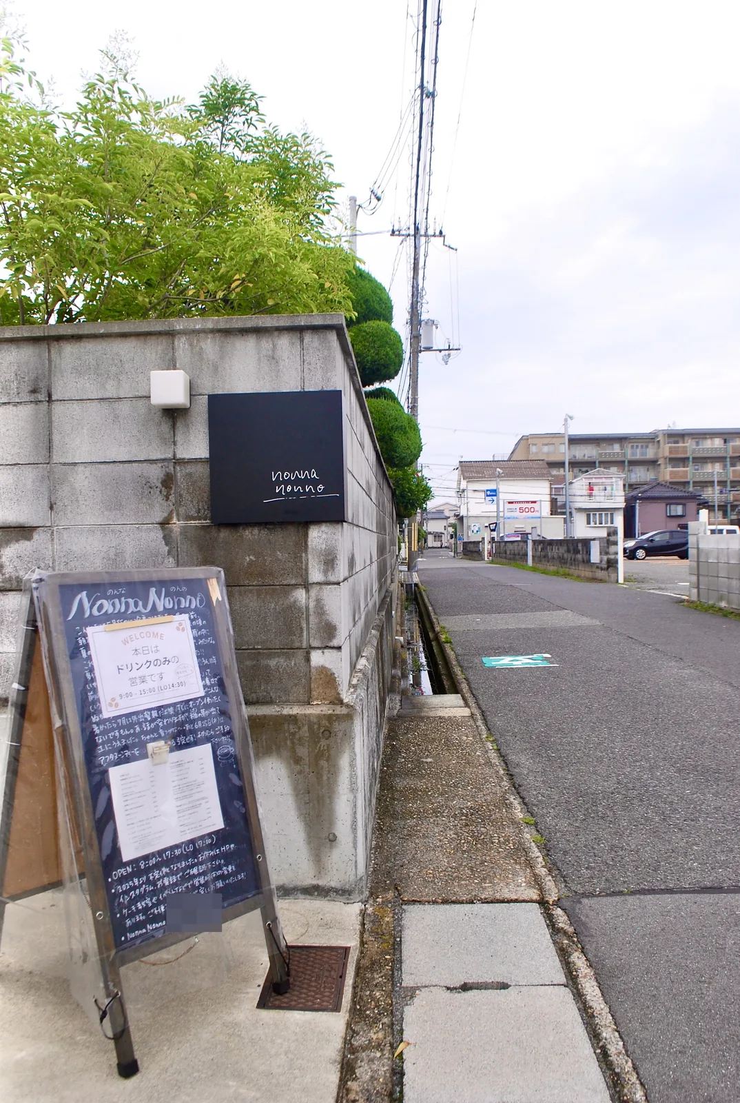 ブロック塀に立てかけたカフェの黒板と、奥へ続くまっすぐな道