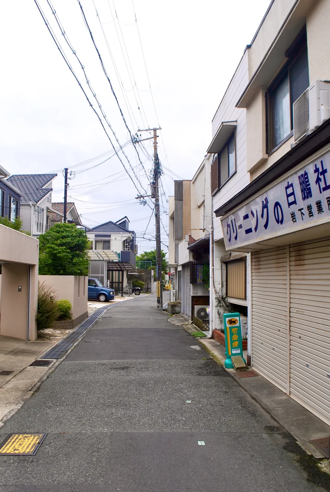 「クリーニングの白鵬社」の看板と、奥へ続く住宅街の道