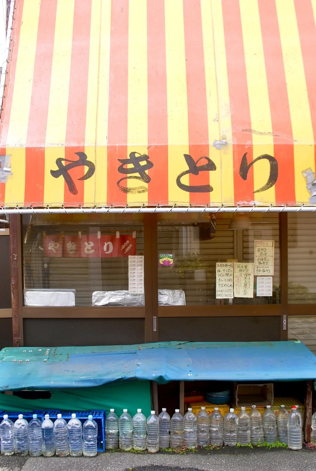 赤と黄色のしましまの日よけに「やきとり」と書かれた店先