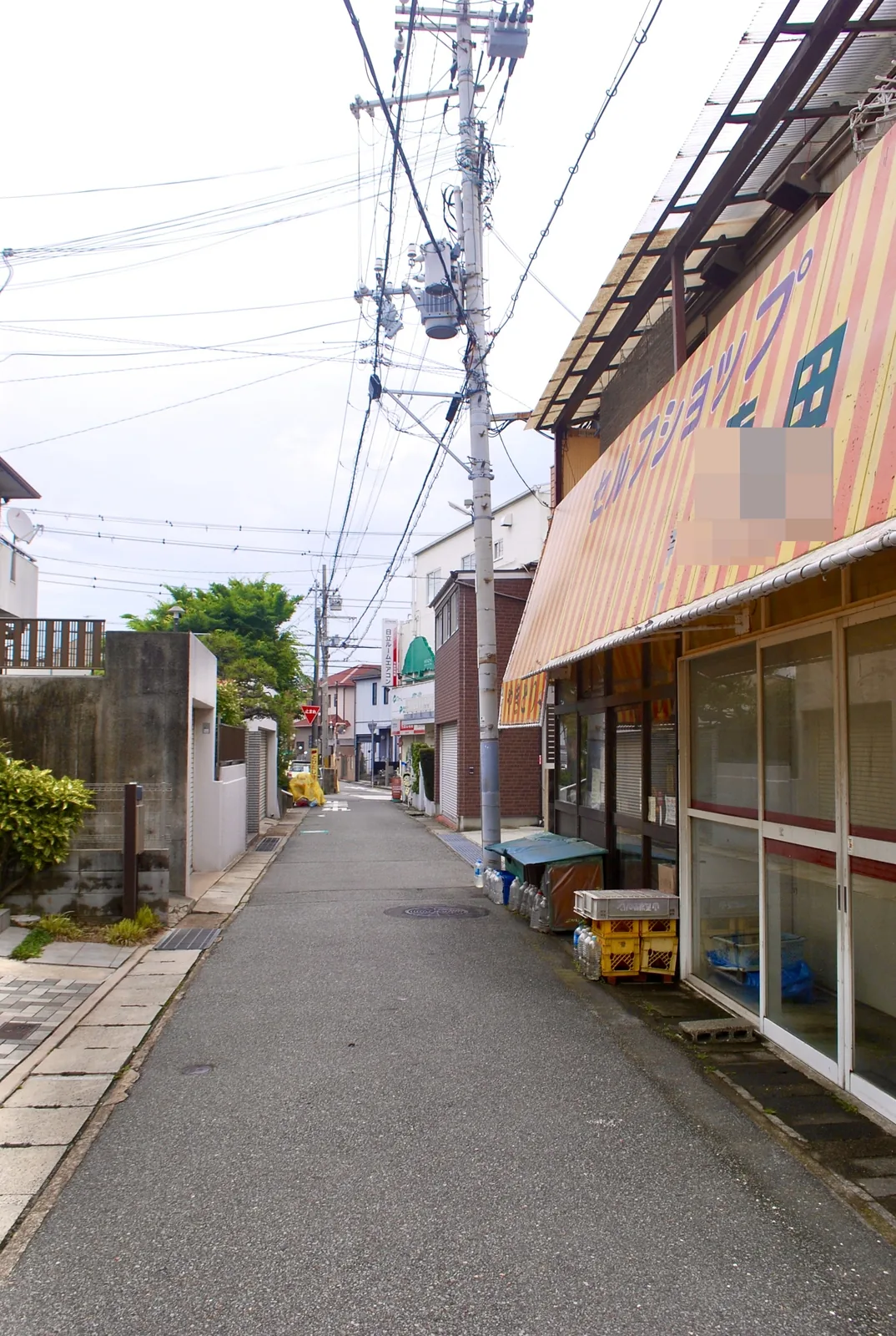 しましまの日よけの商店の前から、奥へまっすぐ続く道