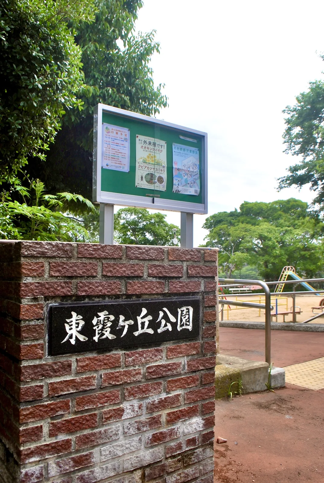 「東霞ケ丘公園」と刻まれたレンガの門と、掲示板のある入口