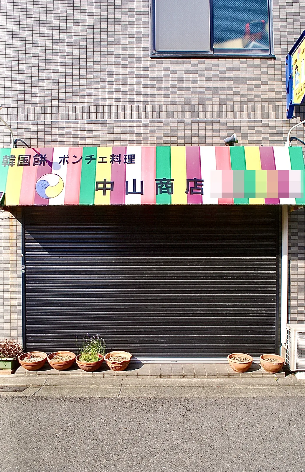 カラフルなしましまの日よけに「韓国餅・ポンチェ料理」と書かれた店