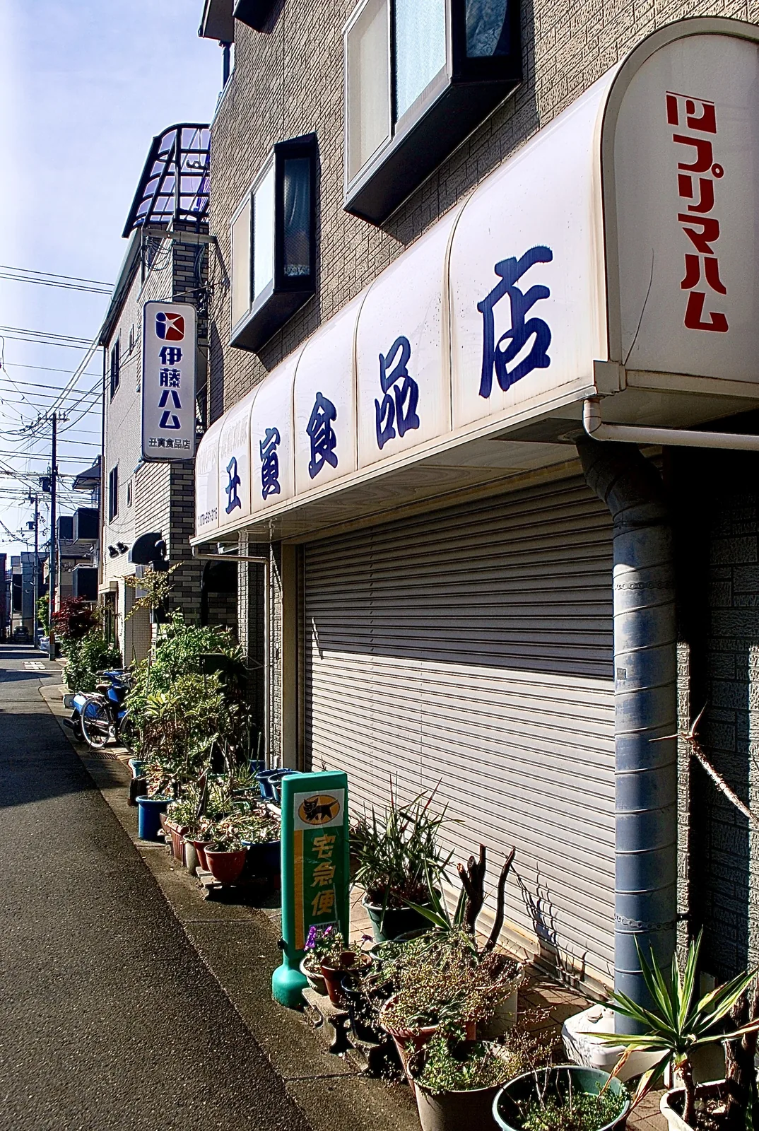 「伊藤ハム」「プリマハム」の看板と、植木鉢の並ぶ食品店