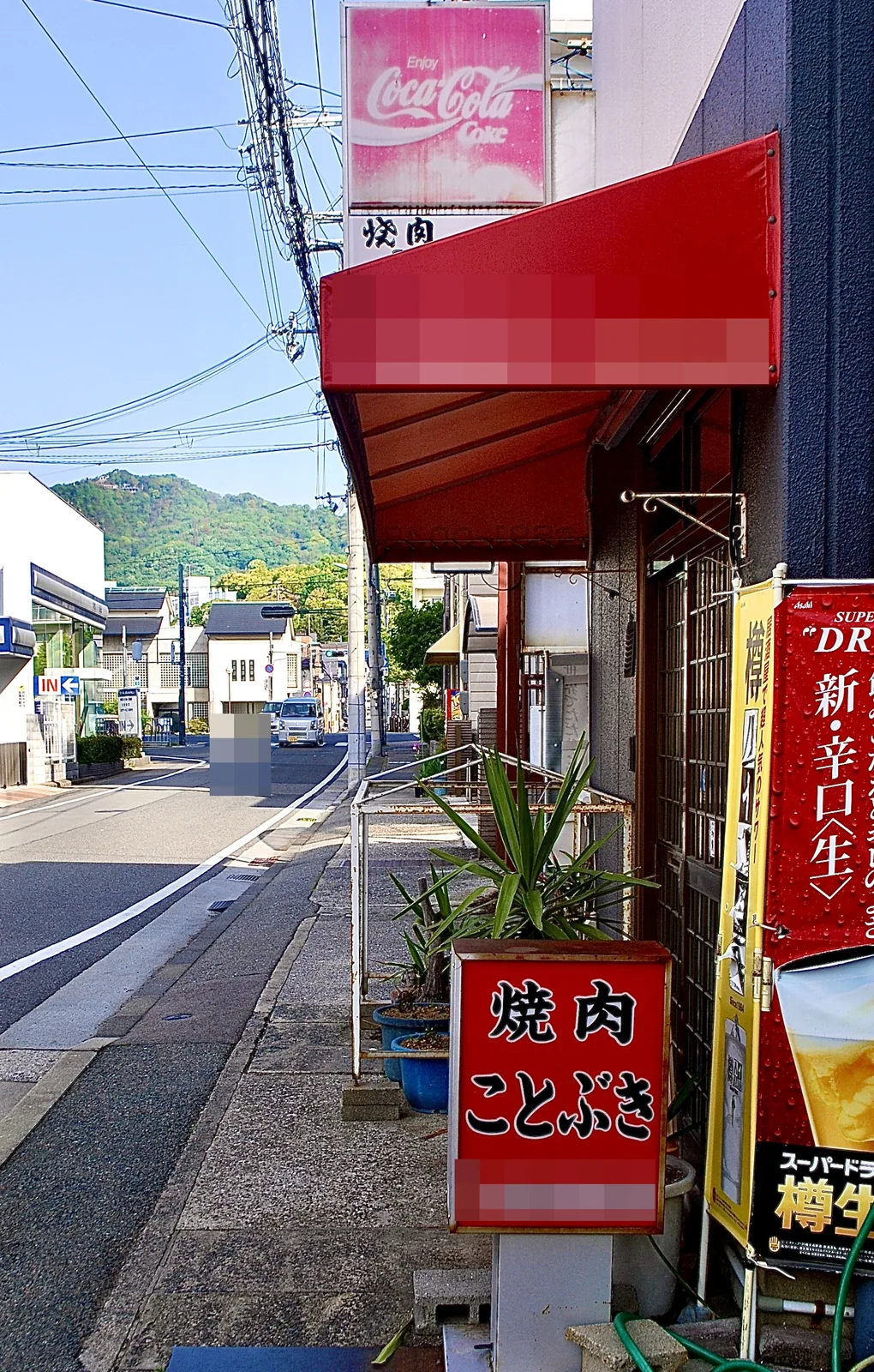「焼肉 ことぶき」の立て看板と、山並みの見える通り