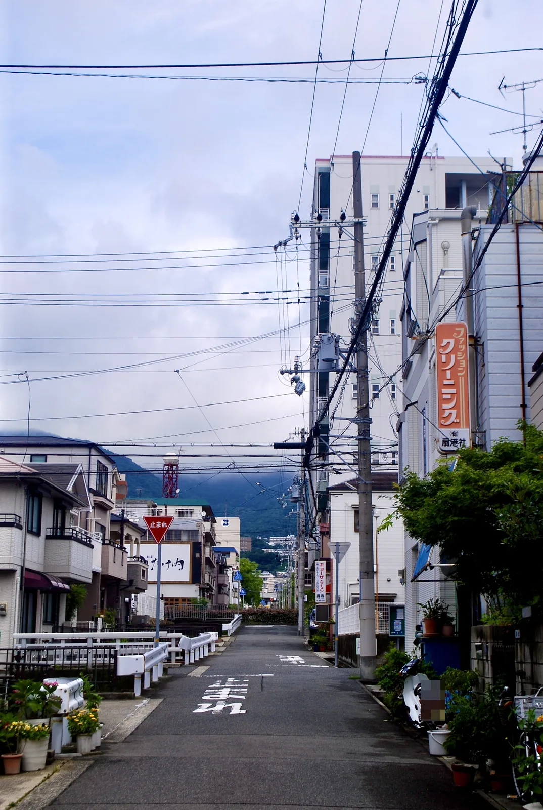 クリーニング店の看板の先に、六甲山の山並みが見える道
