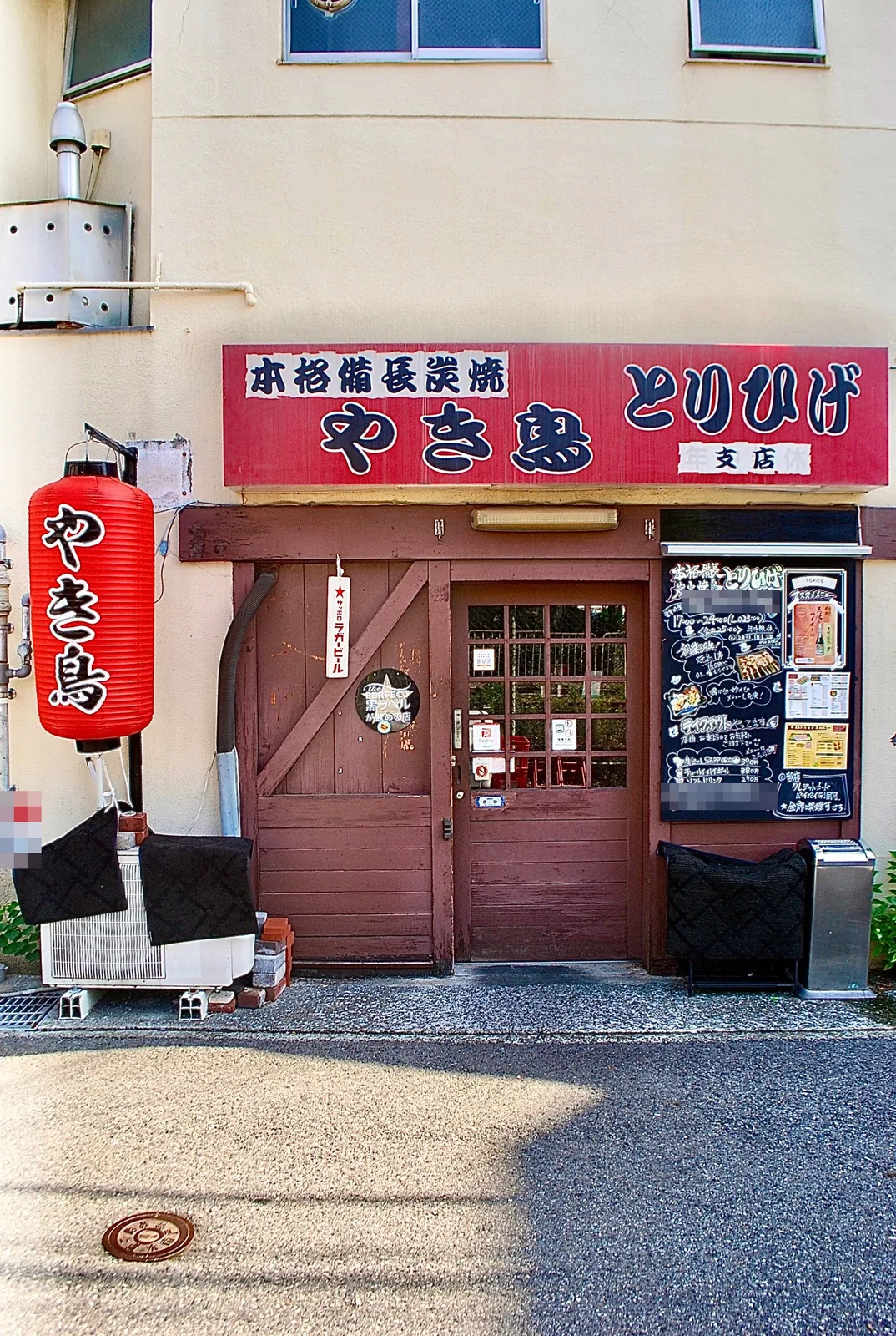 赤い提灯と古い木の扉、手書きの黒板が並ぶ店先