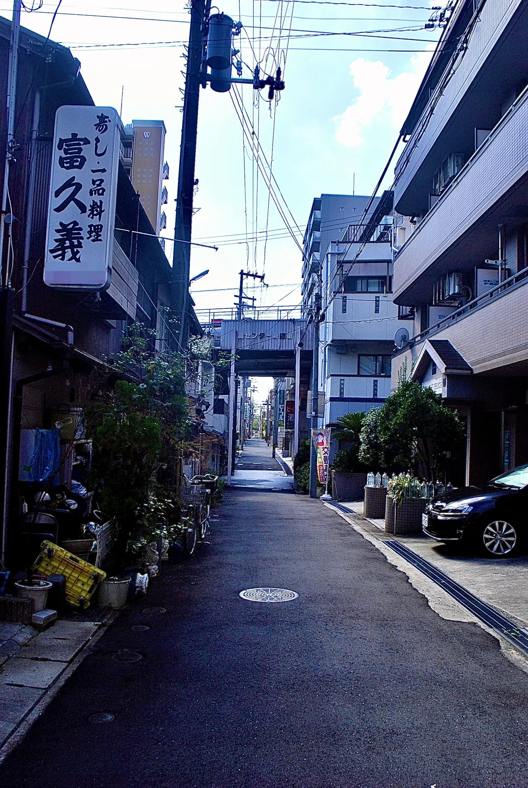 縦長の看板の店の前から、商店街の入口へまっすぐ続く道